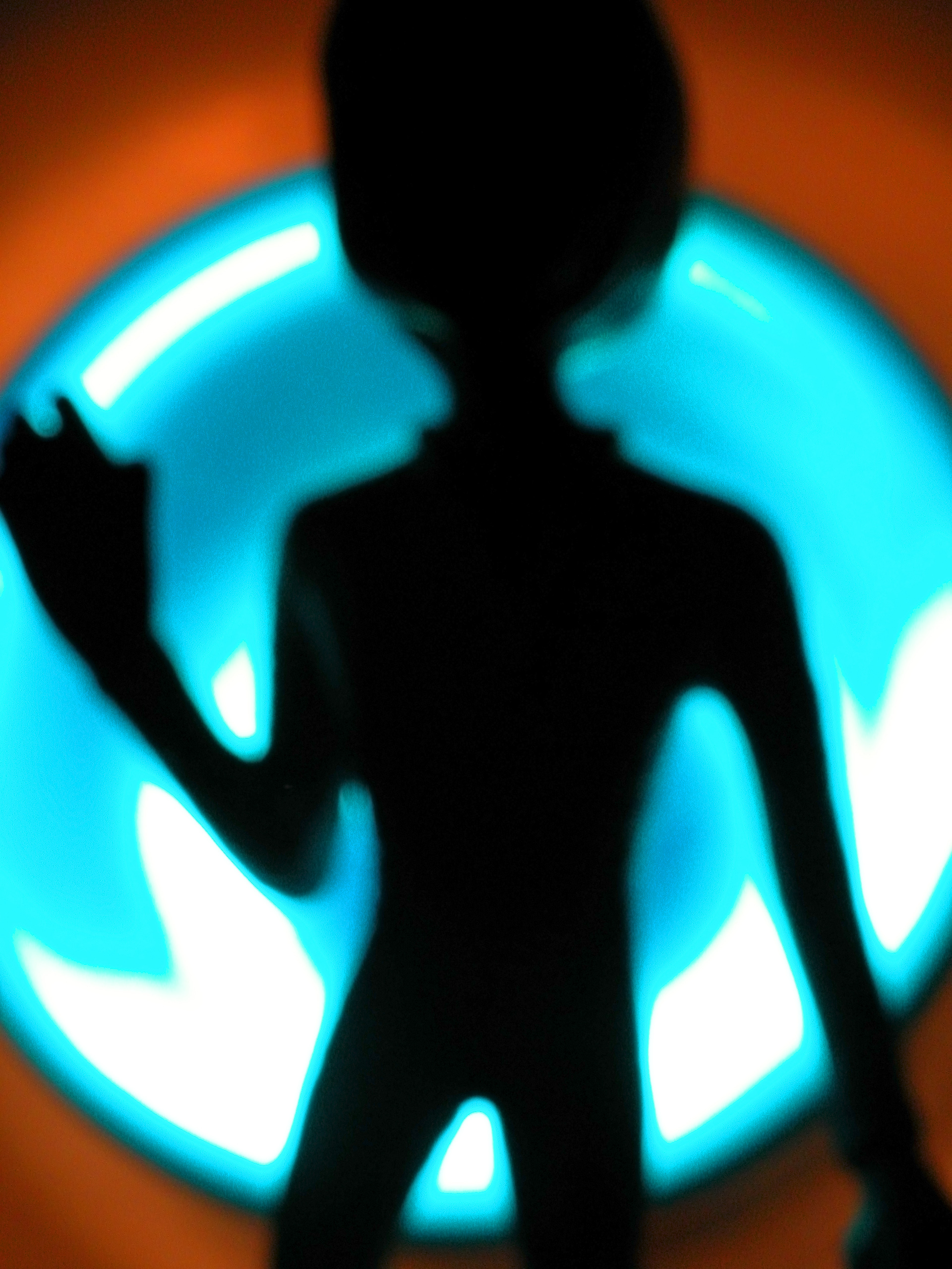 Image Description: The shadow of a being that seems alien. The background is a round, blue light.